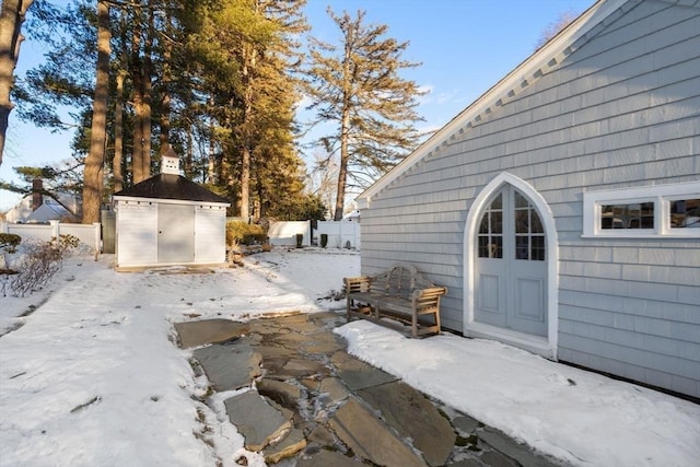 snow covered patio featuring a storage shed, an outdoor structure, and fence