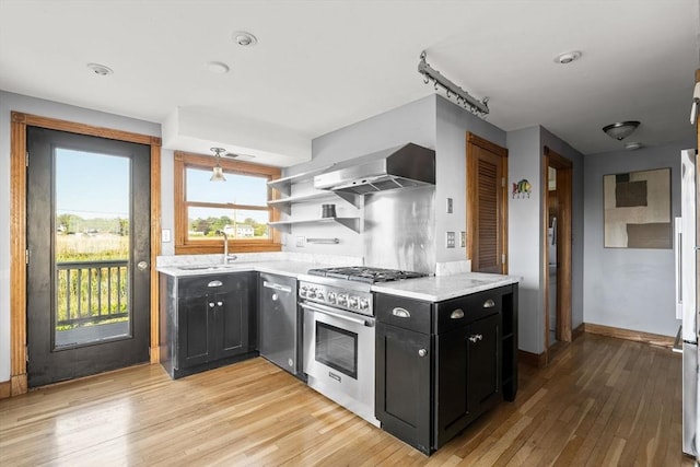 63 Seaside Rd, Scituate, MA 02066 - kitchen featuring appliances with stainless steel finishes, wall chimney range hood, dark cabinets, a sink, and light wood-type flooring