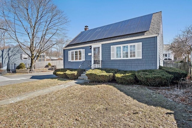 view of front of house featuring roof mounted solar panels, a shingled roof, a chimney, and fence