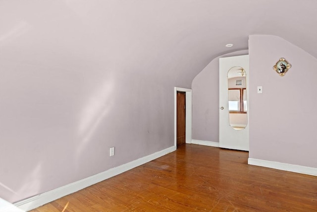 spare room featuring lofted ceiling, baseboards, and wood finished floors