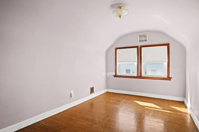 empty room with wood finished floors, visible vents, and baseboards