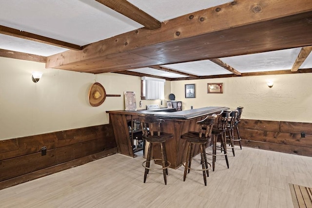 bar featuring a wainscoted wall, wood walls, a dry bar, and beamed ceiling