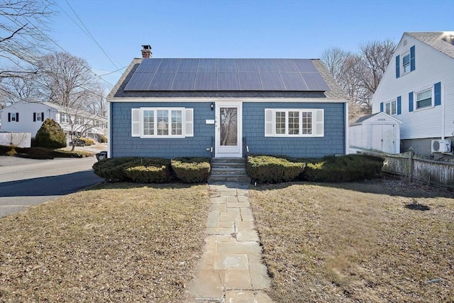 bungalow-style home with a front lawn, entry steps, fence, solar panels, and a chimney