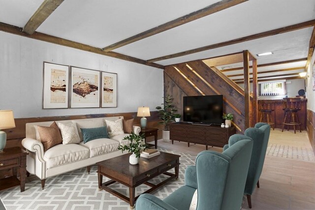 living area featuring light wood-type flooring, beamed ceiling, a bar, and wooden walls