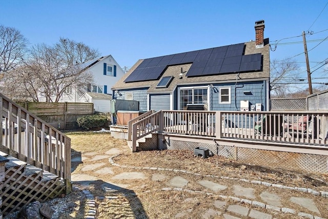 back of property with fence, solar panels, a chimney, a shingled roof, and a deck