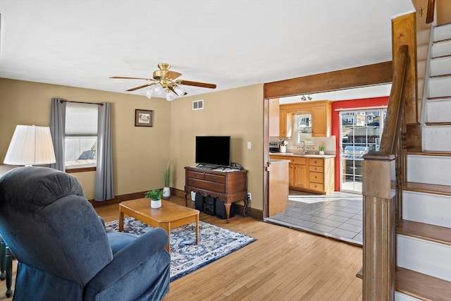 living area featuring light wood-style flooring, a ceiling fan, visible vents, and baseboards