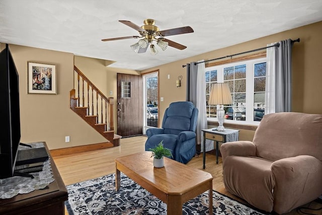 living area with baseboards, stairs, light wood-style floors, and a ceiling fan