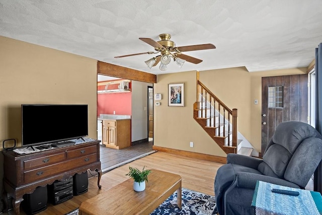 living area with stairway, a ceiling fan, baseboards, light wood-style floors, and a textured ceiling