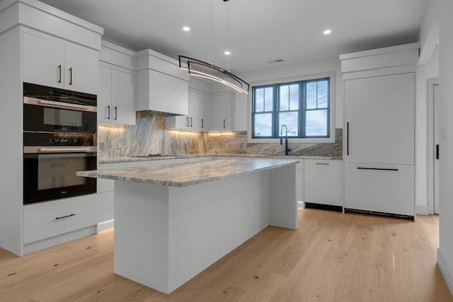 kitchen featuring white cabinetry, a center island, multiple ovens, decorative light fixtures, and light wood-type flooring