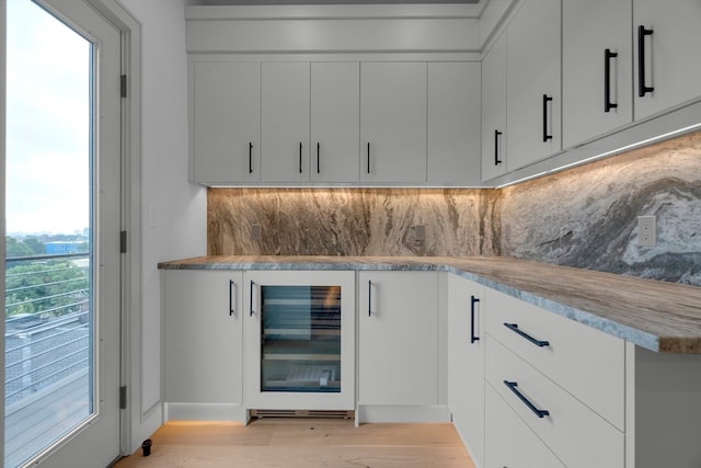 bar with beverage cooler, light wood-type flooring, white cabinetry, and a wealth of natural light