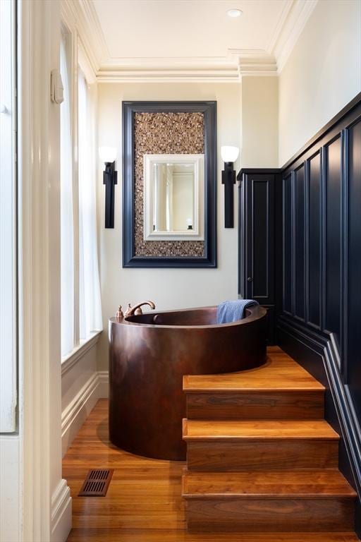 staircase with wood finished floors, ornamental molding, and visible vents