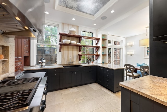 kitchen featuring pendant lighting, kitchen peninsula, sink, a raised ceiling, and wall chimney range hood