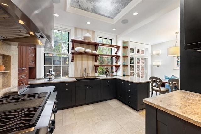 kitchen featuring a tray ceiling, light countertops, a sink, open shelves, and island range hood