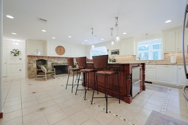 8 Mercer Ln, Franklin, MA 02038 - kitchen featuring stainless steel microwave, decorative backsplash, white cabinetry, a center island, and light stone countertops