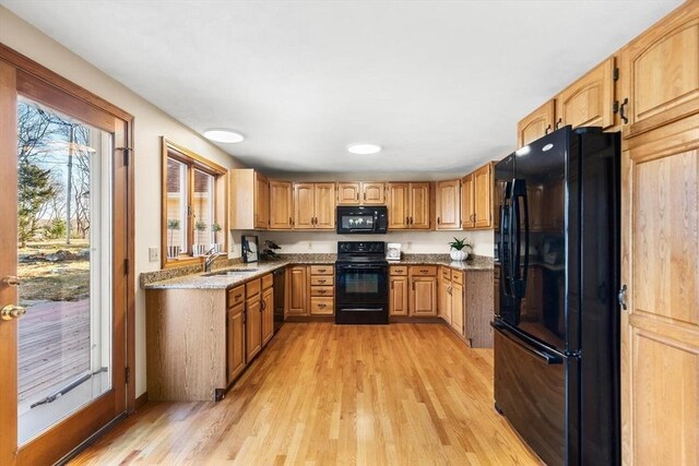 kitchen with black appliances, stone countertops, light wood-type flooring, and sink