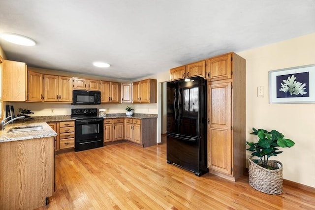 kitchen with black appliances, light hardwood / wood-style floors, dark stone countertops, and sink