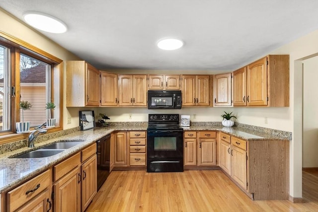 kitchen with light stone counters, sink, black appliances, and light wood-type flooring