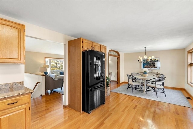 kitchen with pendant lighting, light brown cabinets, black refrigerator, a notable chandelier, and light stone counters