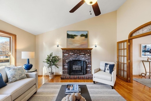 living room with ceiling fan, light hardwood / wood-style flooring, lofted ceiling, and a brick fireplace