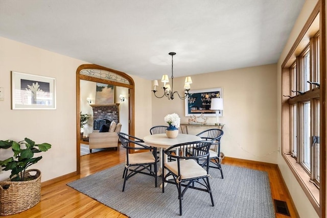 dining room featuring light hardwood / wood-style floors, a brick fireplace, and a notable chandelier