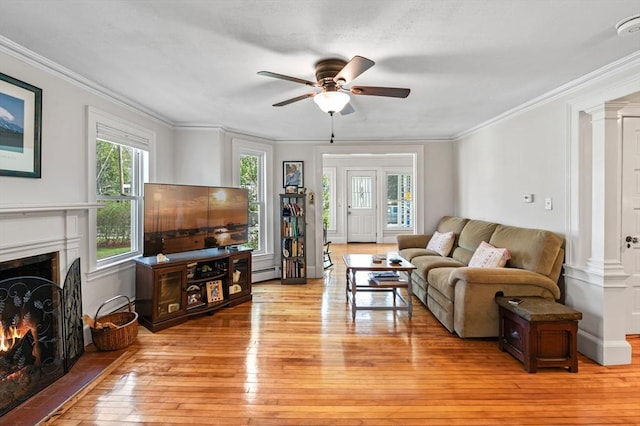 living room with ceiling fan, light wood-type flooring, a baseboard heating unit, a warm lit fireplace, and ornamental molding
