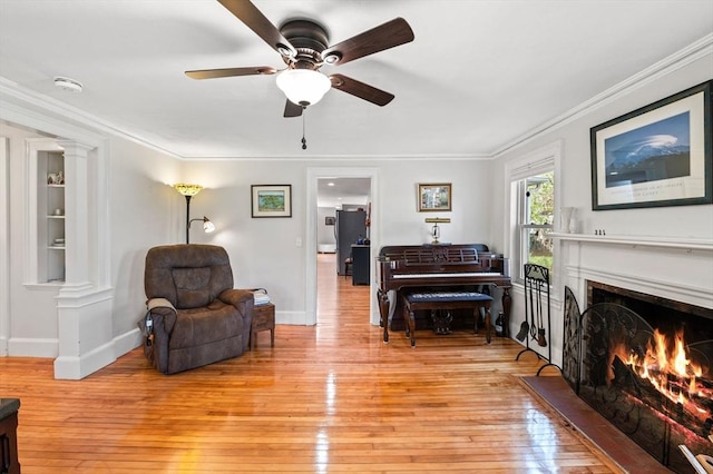 living area with light wood-style floors, ornamental molding, baseboards, and ceiling fan