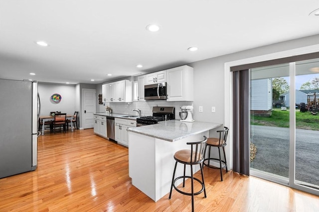 kitchen featuring a breakfast bar, a sink, light wood-style floors, stainless steel appliances, and white cabinetry