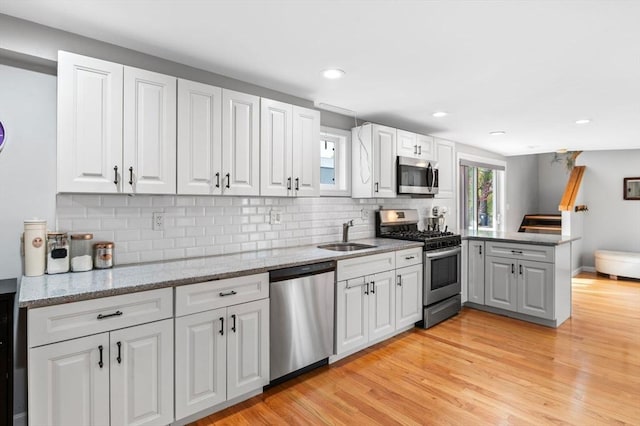 kitchen featuring a sink, stainless steel appliances, a peninsula, light wood-type flooring, and backsplash