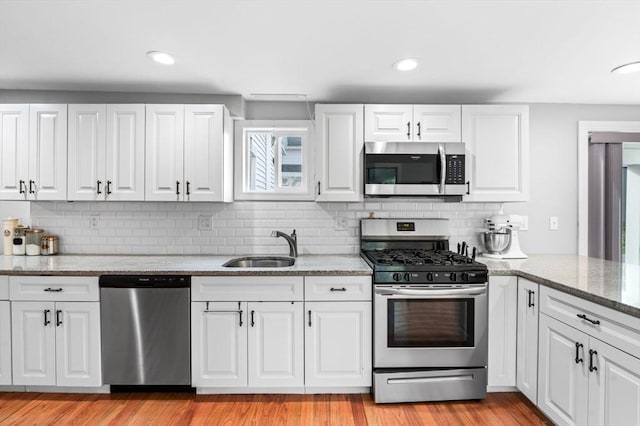 kitchen featuring white cabinets, light stone counters, a sink, stainless steel appliances, and decorative backsplash