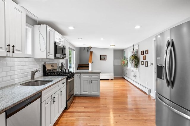 kitchen featuring appliances with stainless steel finishes, a sink, light wood finished floors, a peninsula, and a baseboard radiator