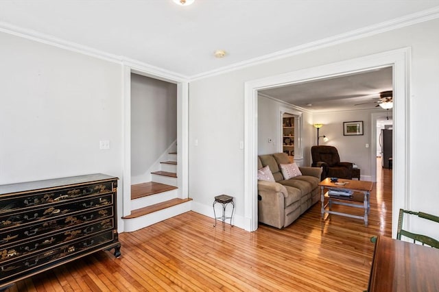 living room with crown molding, ceiling fan, light wood finished floors, stairs, and baseboards