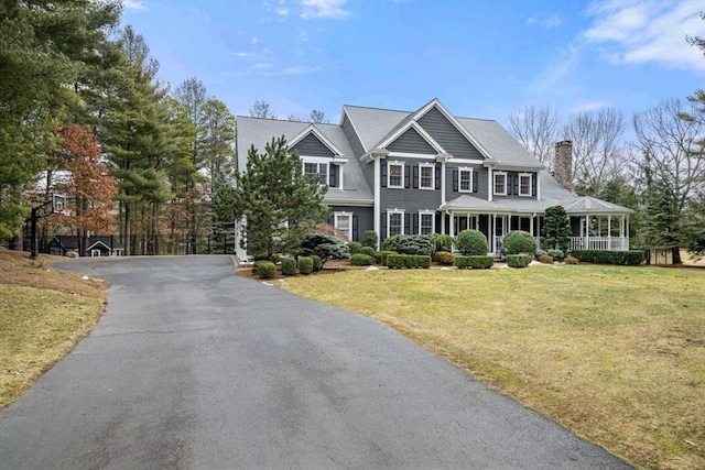 view of front of house with driveway, a chimney, a porch, and a front yard