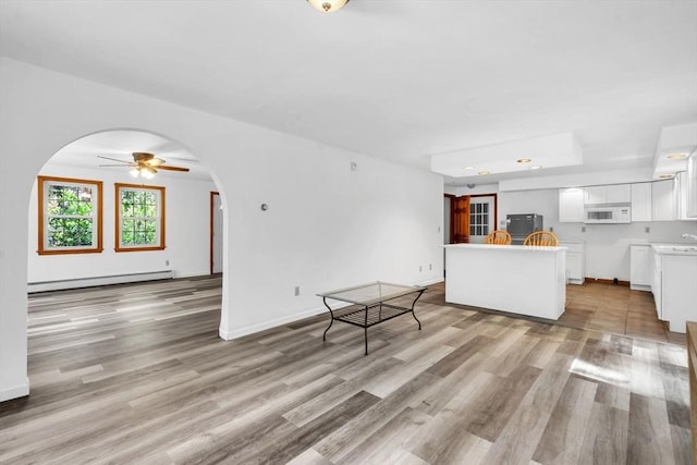 unfurnished living room featuring ceiling fan, a baseboard heating unit, and light hardwood / wood-style flooring