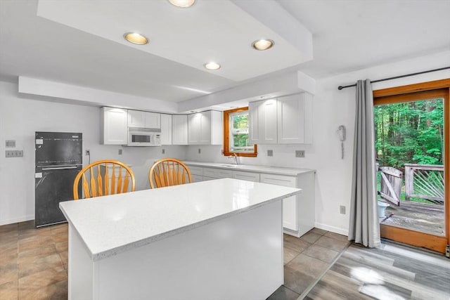 kitchen with sink, white cabinets, black fridge, and a center island