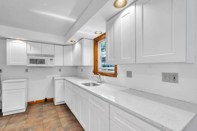 kitchen with light stone countertops, sink, and white cabinets