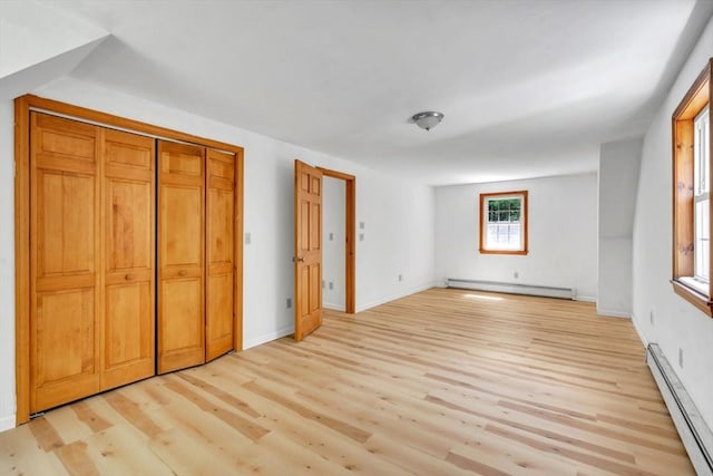 unfurnished bedroom featuring a baseboard heating unit, a closet, and light wood-type flooring