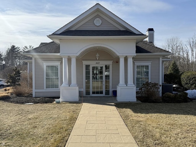 doorway to property with roof with shingles, a chimney, and a yard