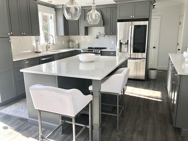 kitchen featuring appliances with stainless steel finishes, gray cabinets, a kitchen island, dark wood finished floors, and a sink