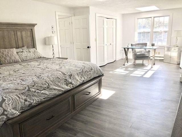bedroom featuring a closet, a baseboard heating unit, and dark wood finished floors