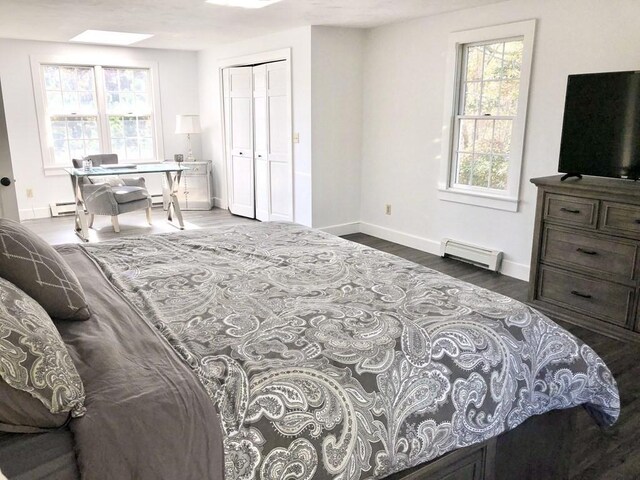 bedroom with a closet, a baseboard radiator, baseboards, and wood finished floors
