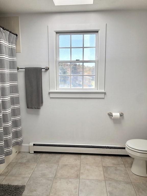 bathroom featuring baseboards, curtained shower, tile patterned floors, toilet, and a baseboard radiator