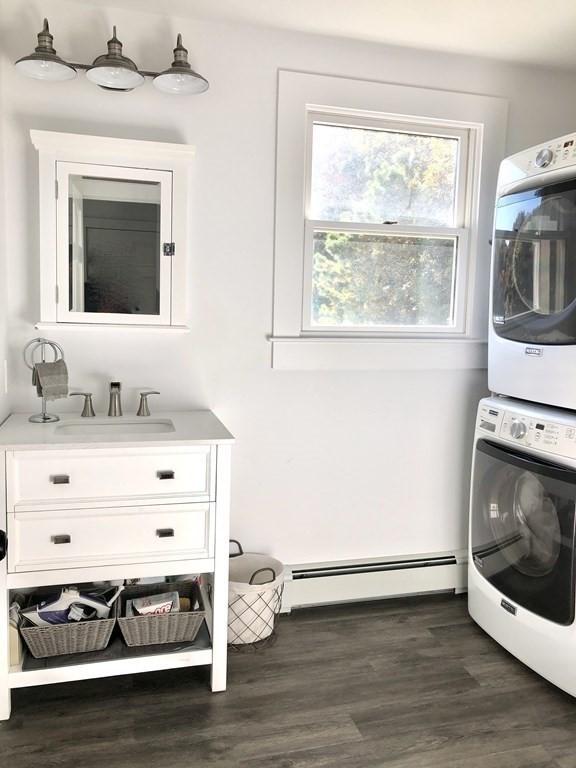 clothes washing area with a baseboard radiator, dark wood-style flooring, a sink, and stacked washer / drying machine