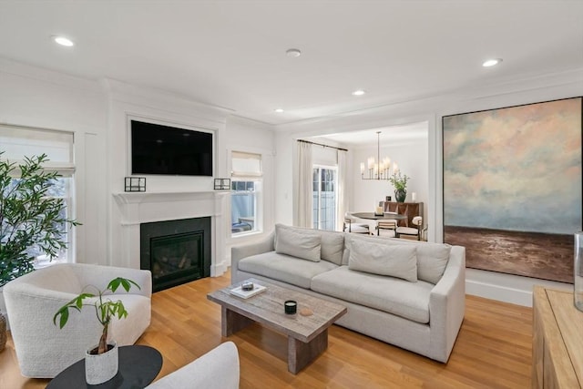 living room featuring a chandelier, a glass covered fireplace, ornamental molding, recessed lighting, and light wood-style flooring