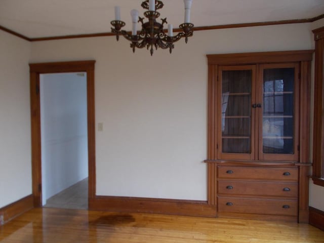 spare room featuring a chandelier, light hardwood / wood-style floors, and ornamental molding