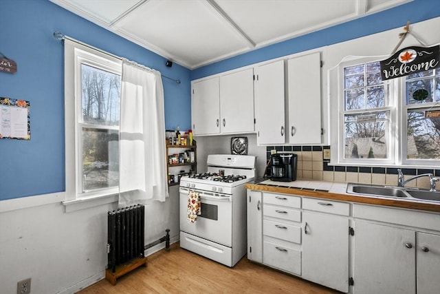 kitchen with tasteful backsplash, sink, radiator, white range with gas stovetop, and white cabinets