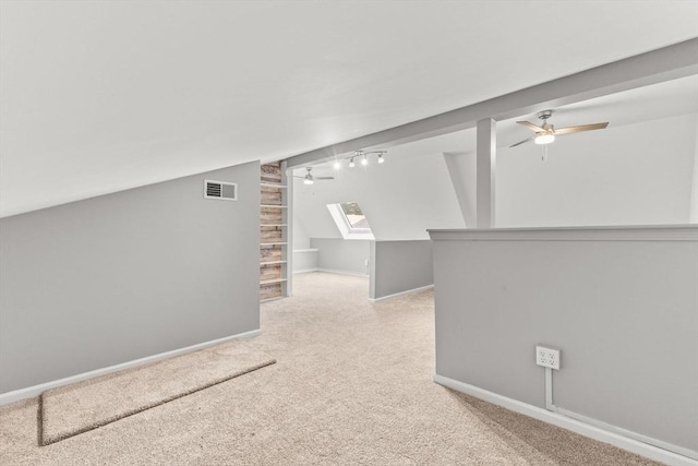 interior space featuring ceiling fan, vaulted ceiling with skylight, and light carpet