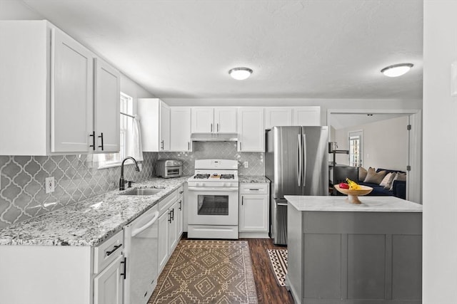 kitchen featuring white gas stove, under cabinet range hood, dishwashing machine, freestanding refrigerator, and a sink