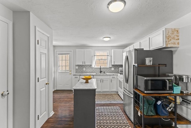 kitchen with a sink, white cabinets, stainless steel microwave, backsplash, and a center island