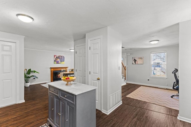 interior space featuring dark wood-type flooring, baseboards, open floor plan, and a warm lit fireplace