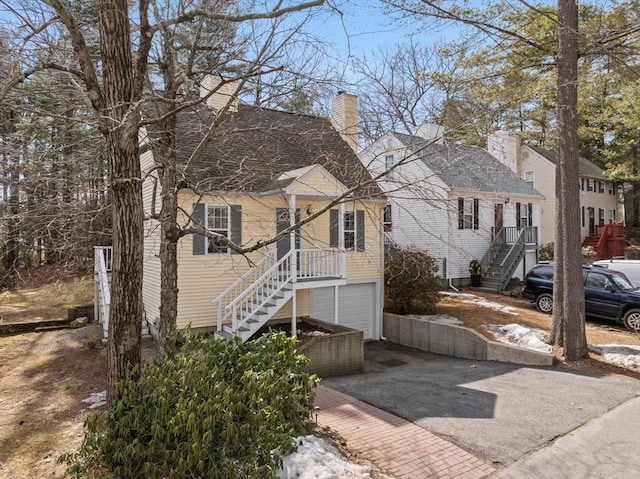 view of front of property featuring aphalt driveway, stairway, a residential view, a chimney, and an attached garage